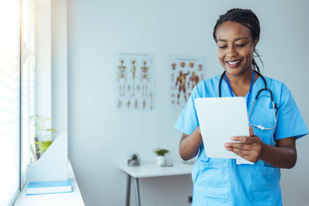 A clinician in scrubs reviewing a patient record on a tablet in a bright clinic
